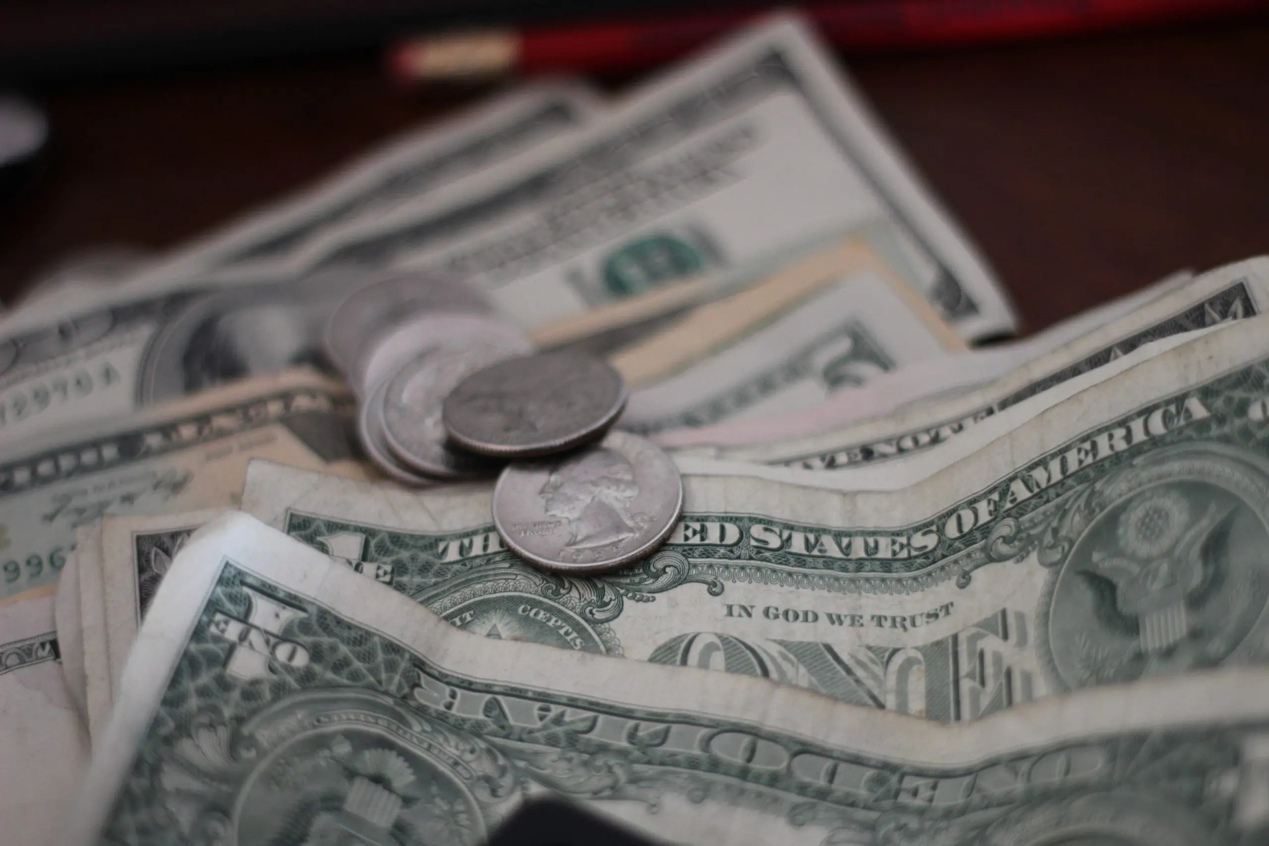 Several U.S. dollar bills are spread out in a line on a wooden surface. There are also some silver coins on top of the dollar bills.