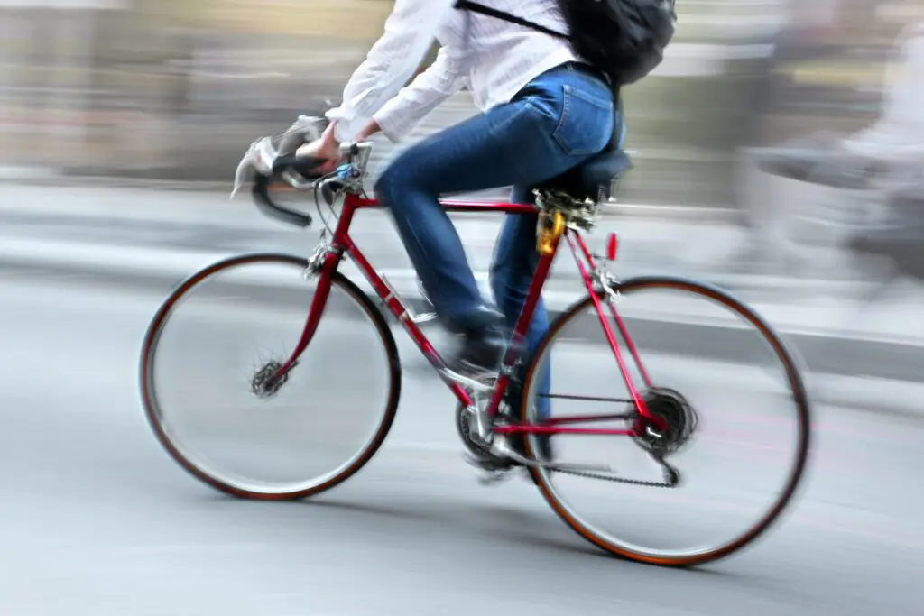 A cyclist wearing a white shirt and jeans is riding a red bicycle.