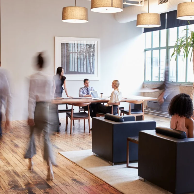 Three people walking around the workplace. A group of three workers are seated together, and one woman is seated alone with her laptop.