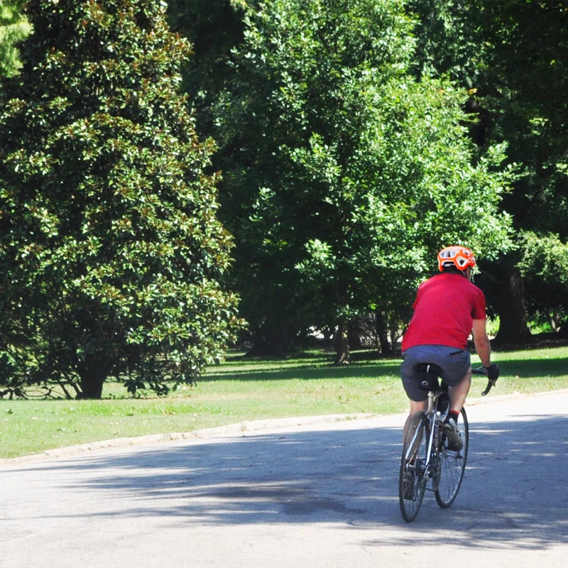 Person in a red shirt and red helmet riding their bike on a trail. Many trees are in the background.