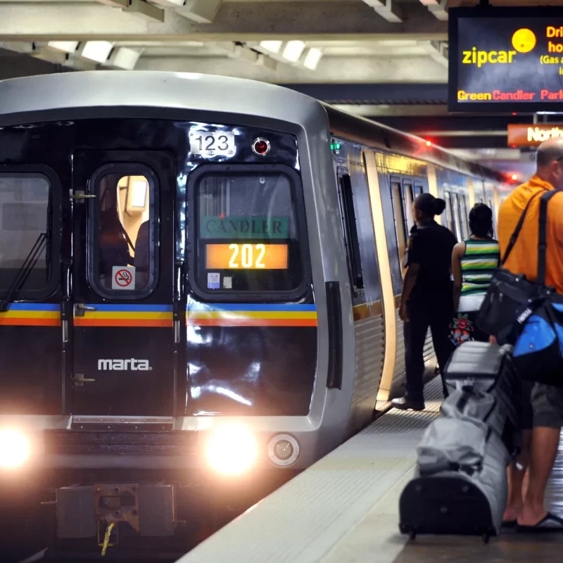 A MARTA train is pulling into its station as several people wait around with their bags or start to board.