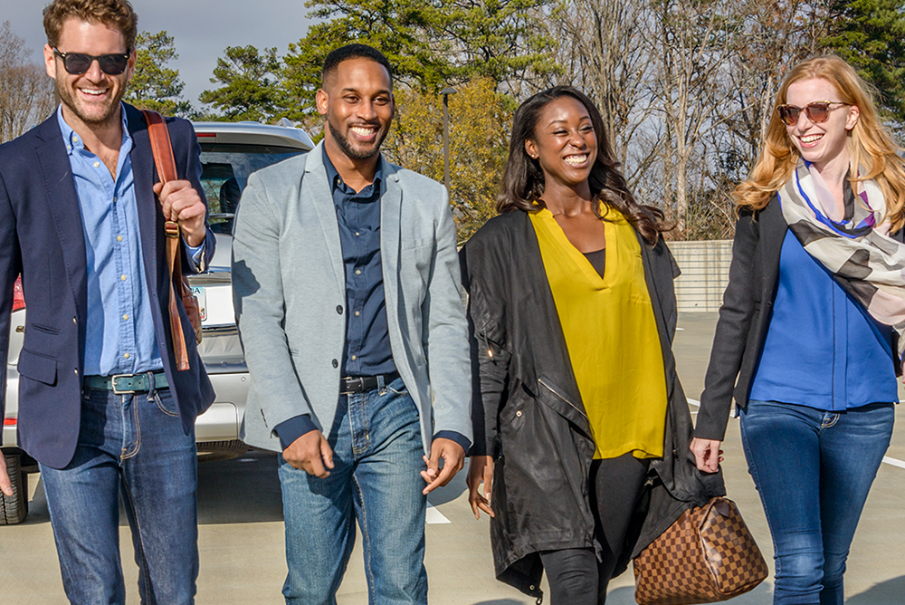Two men and two women wearing business casual clothes are walking outside together and smiling.