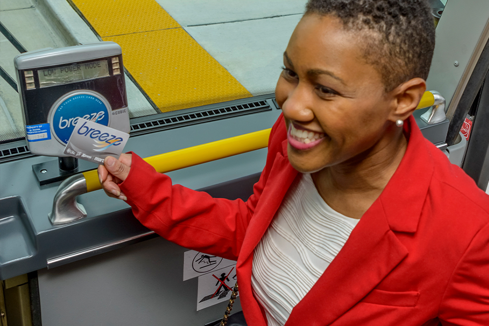 A smiling female commuter is stepping onto a bus holding her Breeze card.