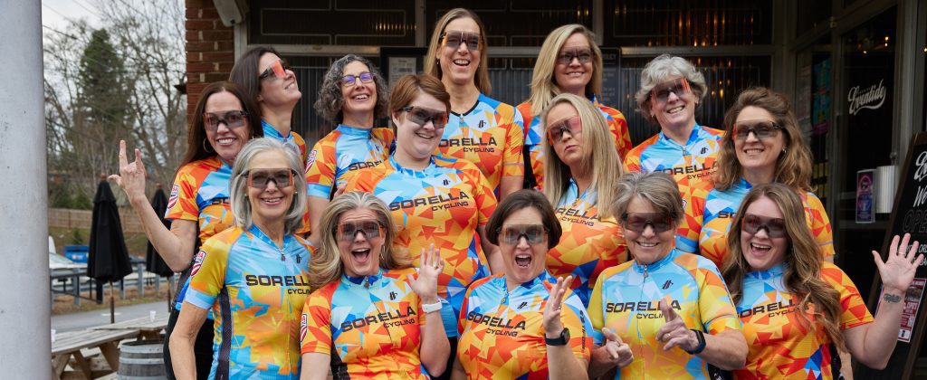 Cyclists from Sorella Cycling, an all-womens cycling club in Atlanta pose for a photo wearing their brightly-colored cycling gear.