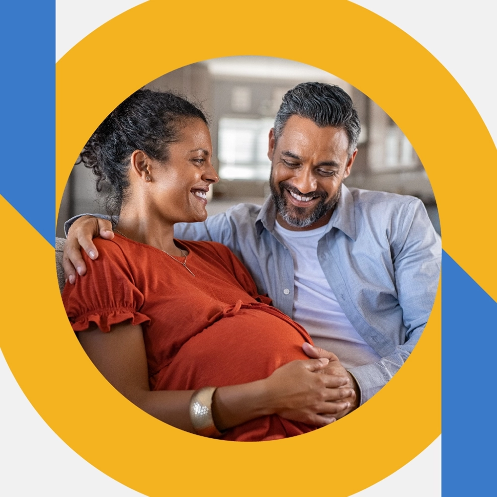 A man and pregnant woman are smiling as they both lay a hand on her stomach.