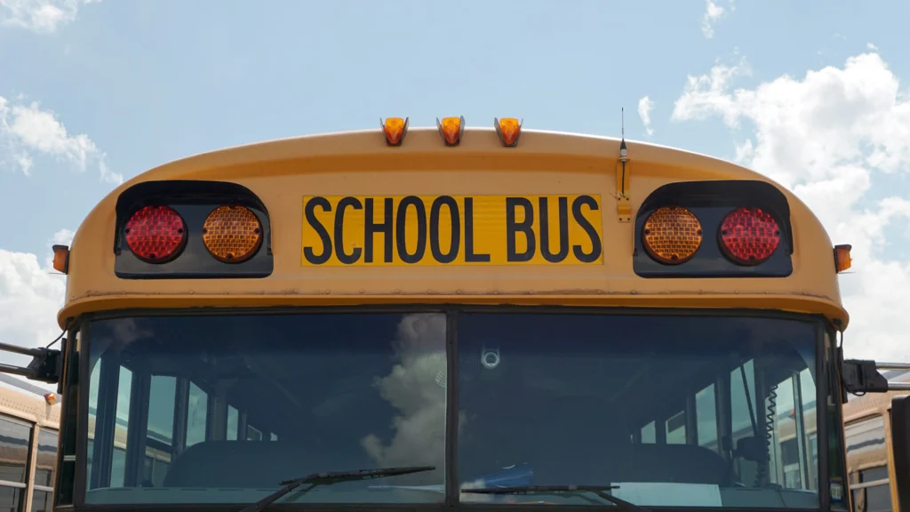 Close-up of the front of a school bus with a cloudy, blue sky in the background.