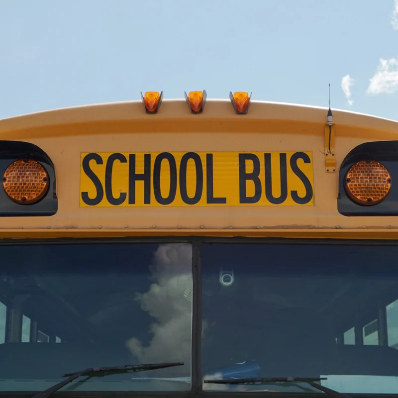 Close-up of the front of a school bus with a cloudy, blue sky in the background.