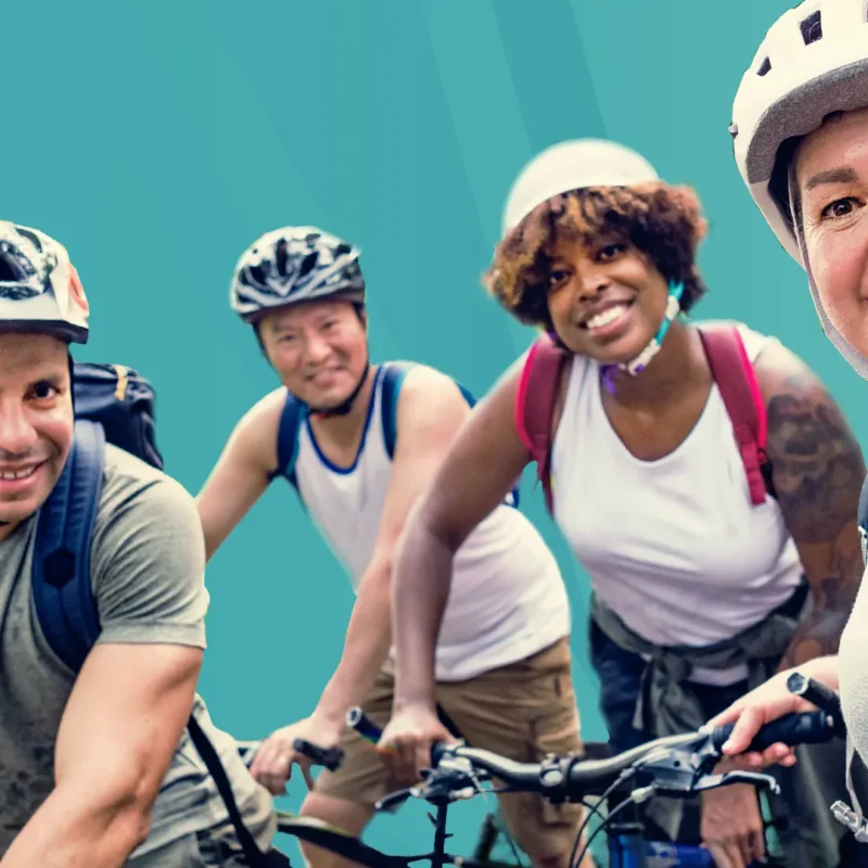 Four adults on bikes, wearing bike helmets, smile for a photo.