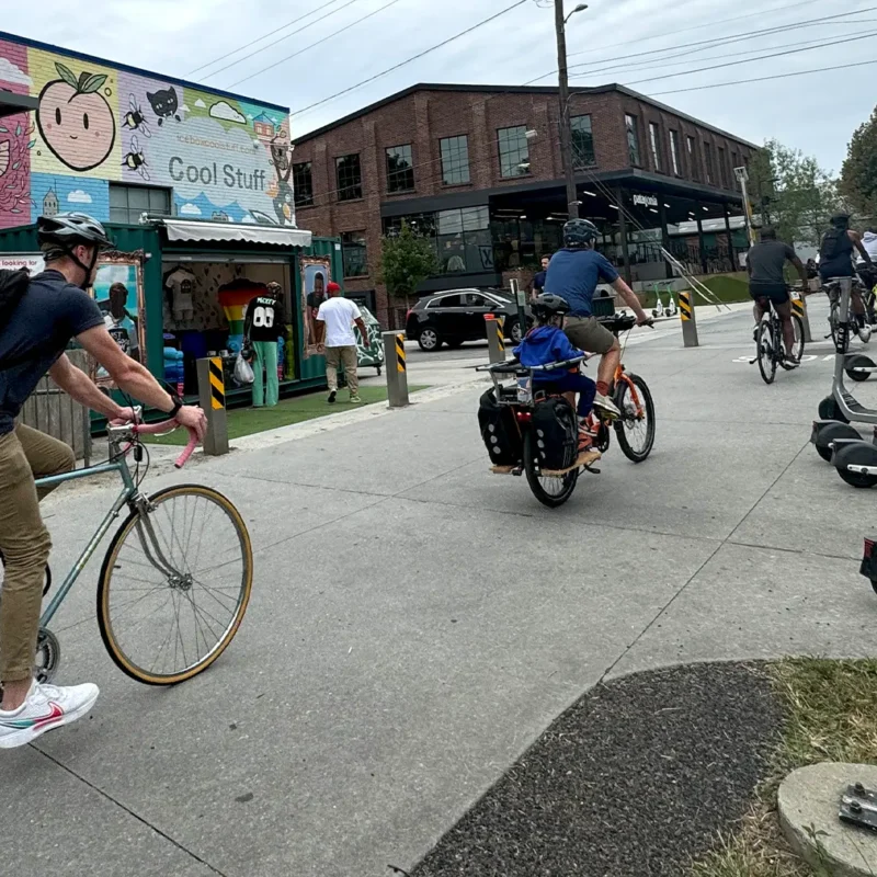 Multiple cyclists ride bikes down walkway through city intersection.