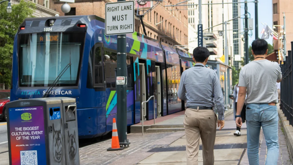 Two people are walking down a street, there is an Atlanta street car passing by them.