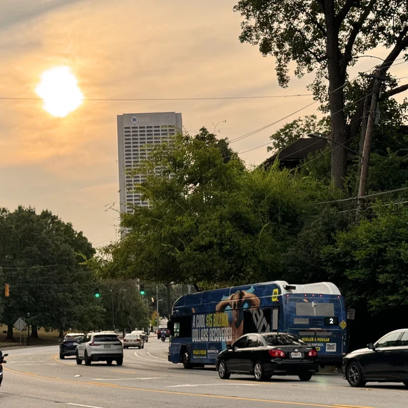 Image of the Atlanta skyline there are several cars driving down the road and a motor cyclist.