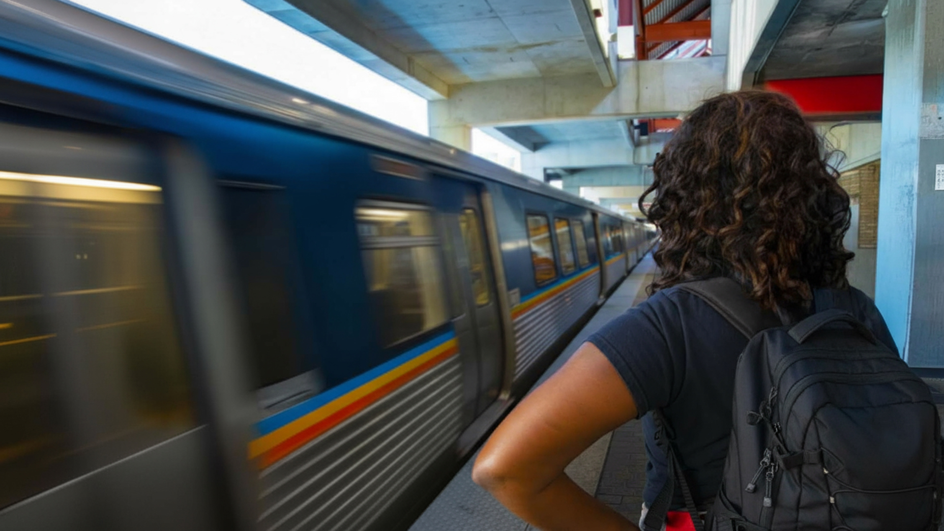 A young woman with a backpack is waiting as a train pulls into the station.