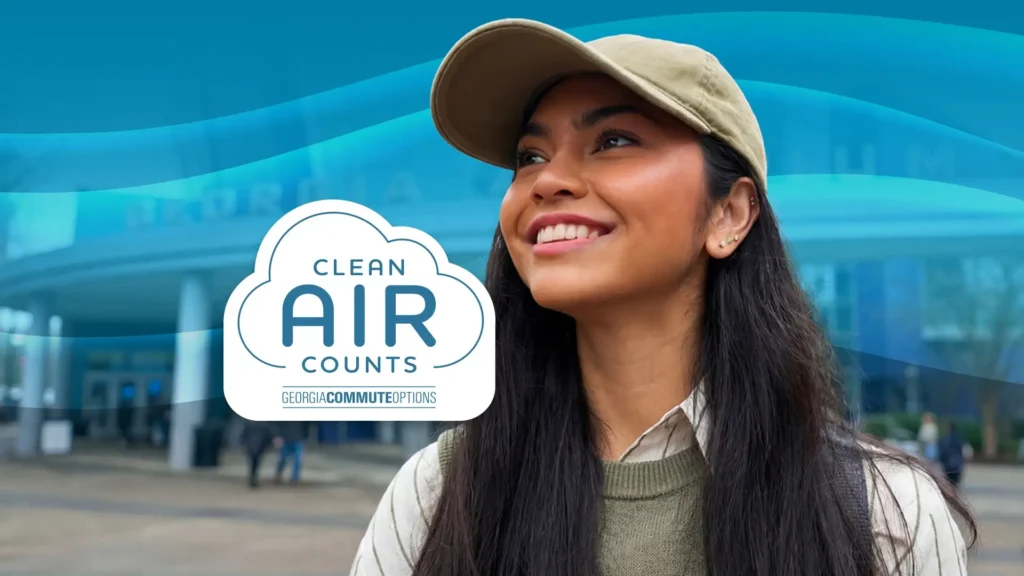 A smiling woman wearing a tan cap looks upward outside a building. In front of her is a cloud-shaped logo that reads "Clean Air Counts, Georgia Commute Options" with blue wavy lines in the background.