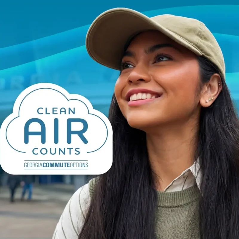 A smiling woman wearing a tan cap looks upward outside a building. In front of her is a cloud-shaped logo that reads "Clean Air Counts, Georgia Commute Options" with blue wavy lines in the background.