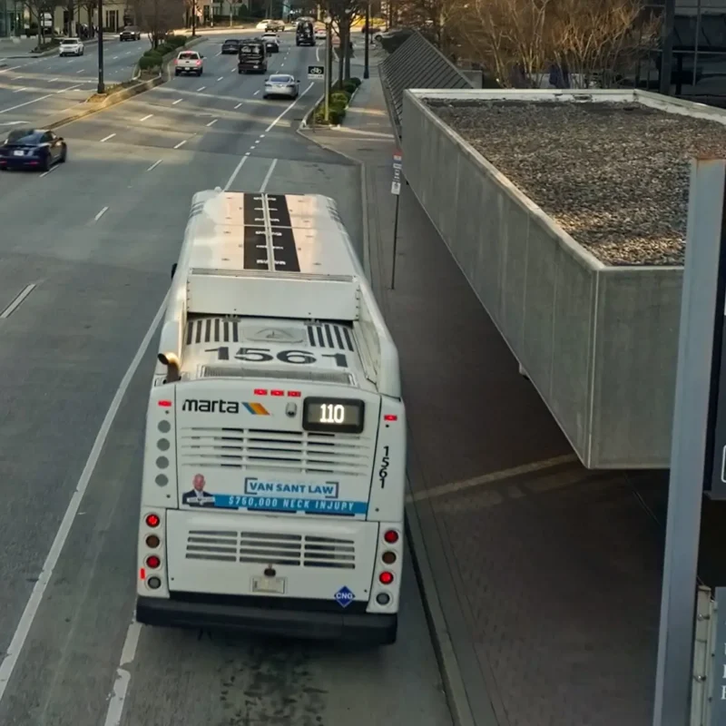 A MARTA bus numbered 1567 is stopped at the Buckhead Transit Station on a city street. Several cars are driving on the road, and a MARTA sign with station information is visible in the foreground.