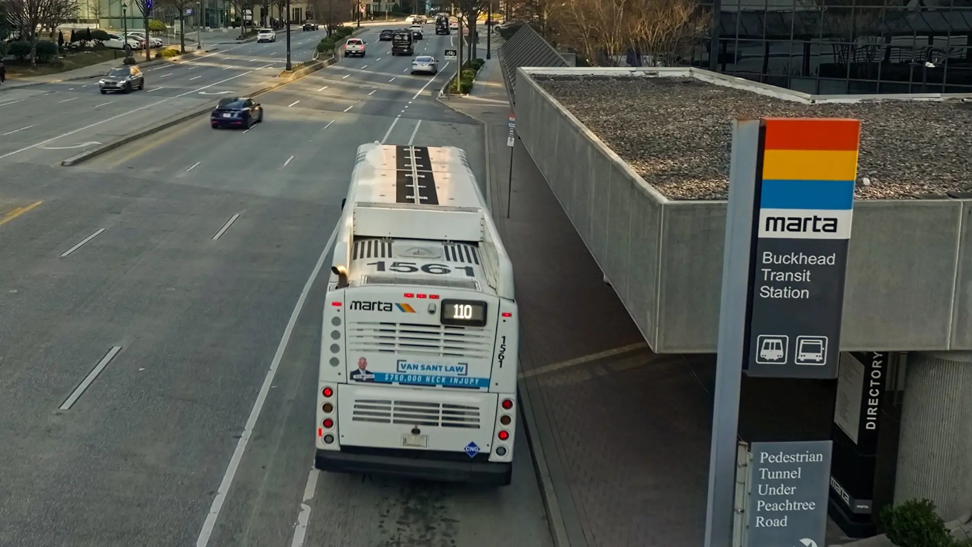 A MARTA bus numbered 1567 is stopped at the Buckhead Transit Station on a city street. Several cars are driving on the road, and a MARTA sign with station information is visible in the foreground.