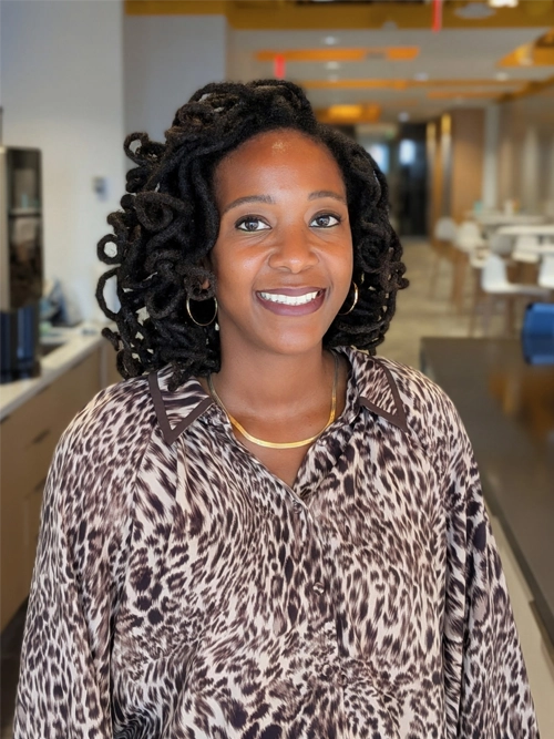 A woman with dark curly hair and hoop earrings wearing a leopard-print button-down shirt and gold chain necklace.
